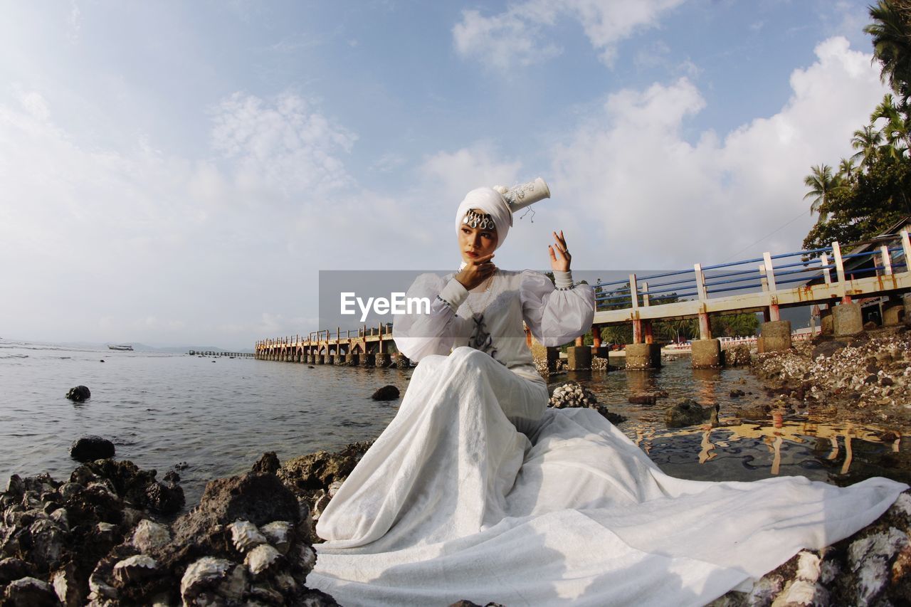 Woman in white dress sitting on rock by sea