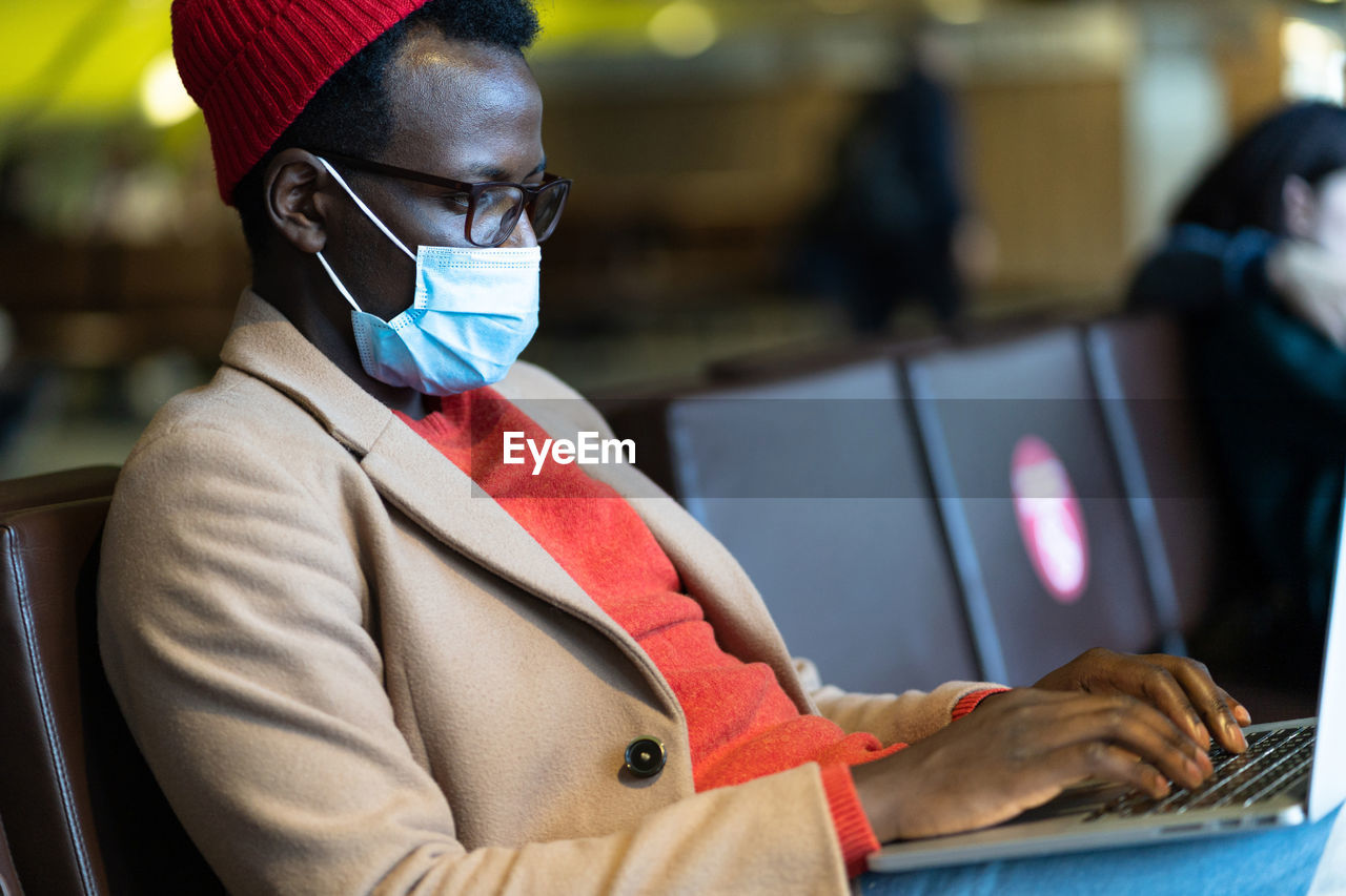 Young businessman wearing mask using laptop while sitting at airport