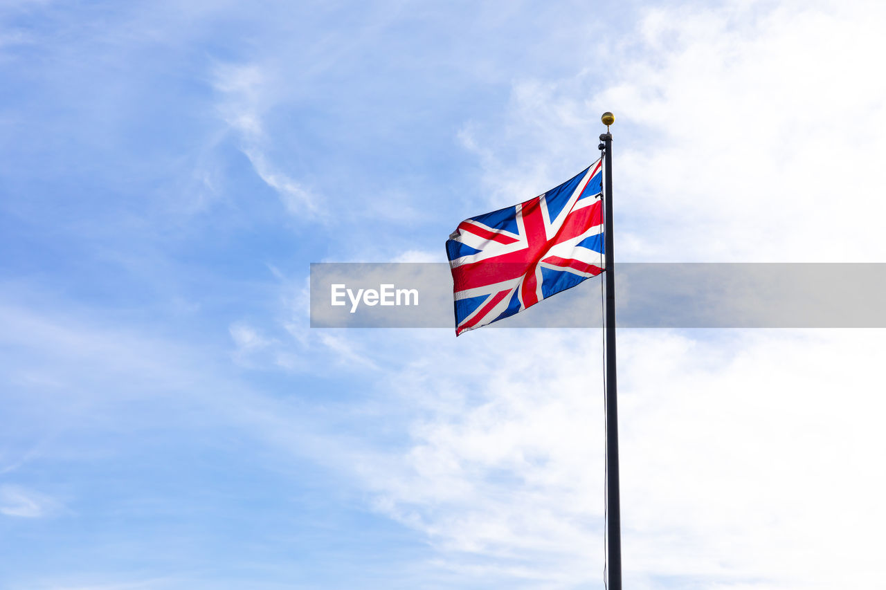 Mockup union jack flag of the united kingdom flying on a flagpole against a minimalistic blue sky
