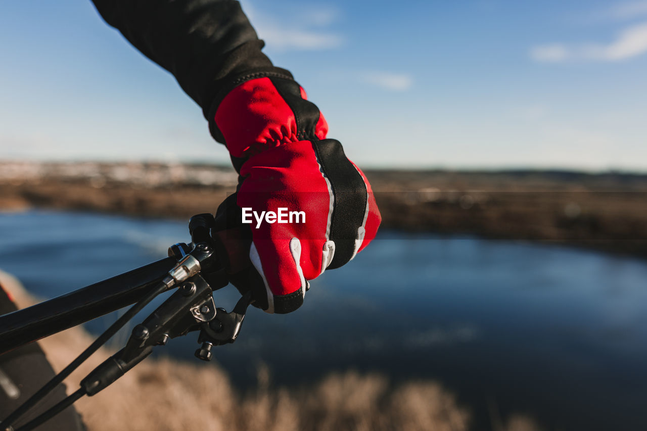 Cropped hand of person riding bicycle by river against sky