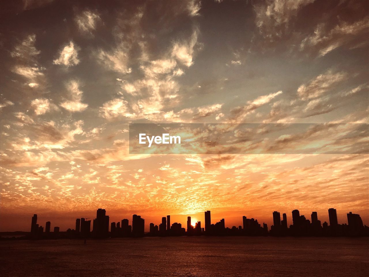 SILHOUETTE BUILDINGS BY SEA AGAINST ROMANTIC SKY