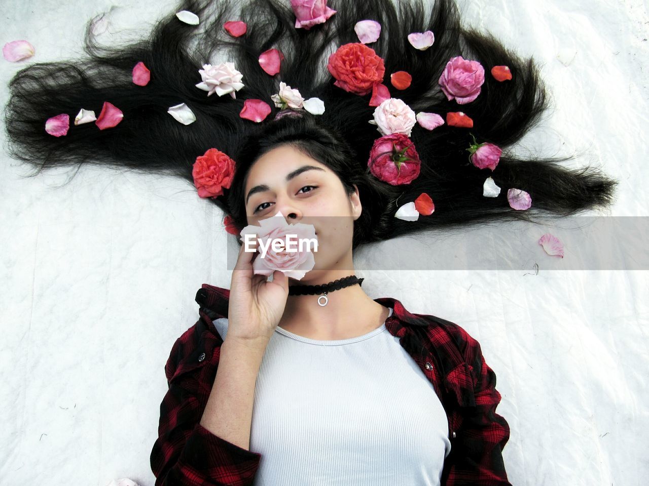 High angle portrait of young woman with flowers lying on bed