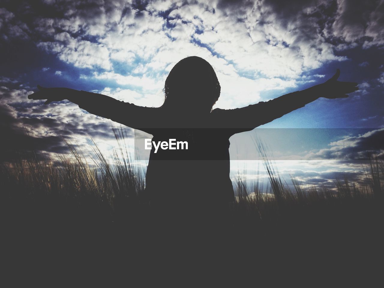 Silhouette woman standing arms outstretched in field