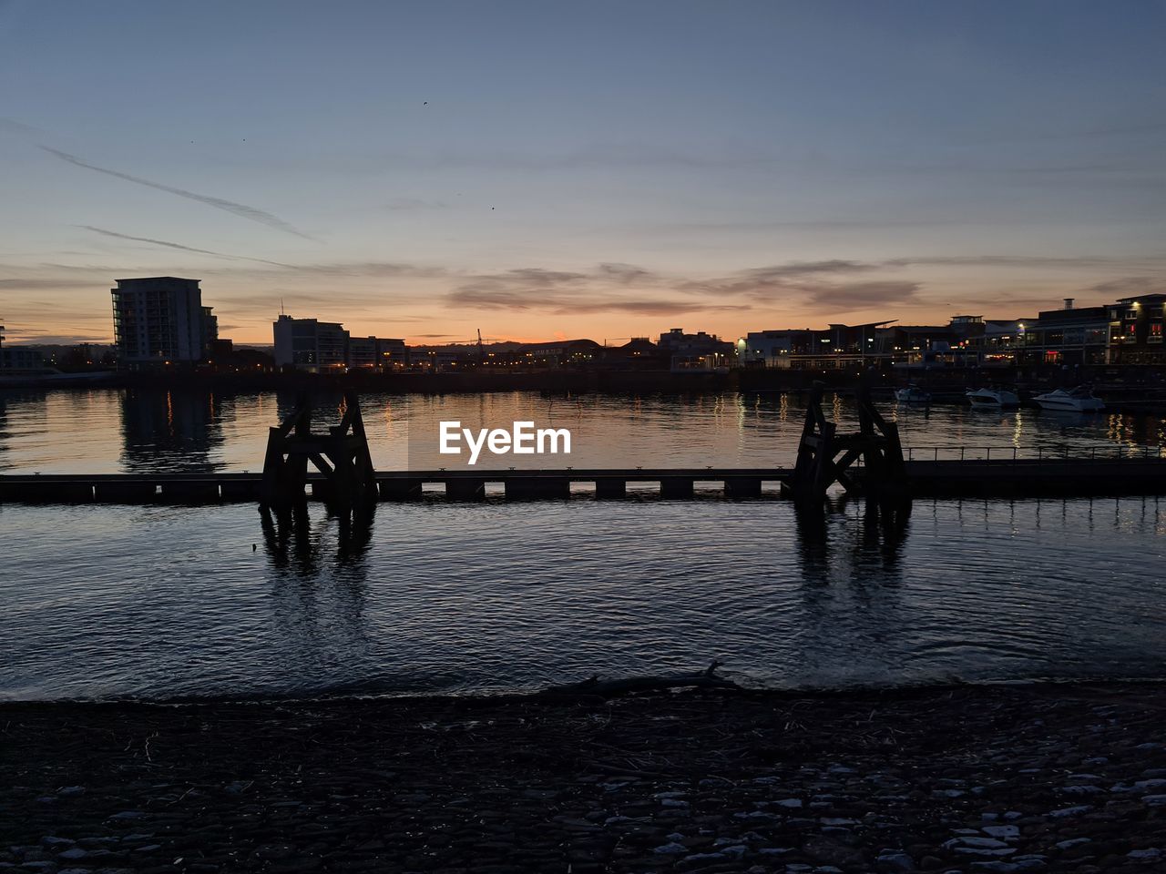 Silhouette people on river against buildings at sunset