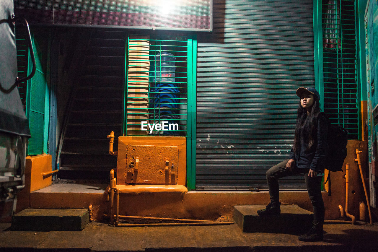 Portrait of woman standing by illuminated building at night