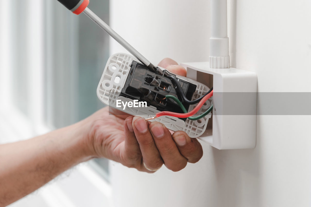 Cropped hands of male electrician repairing electrical outlet on wall