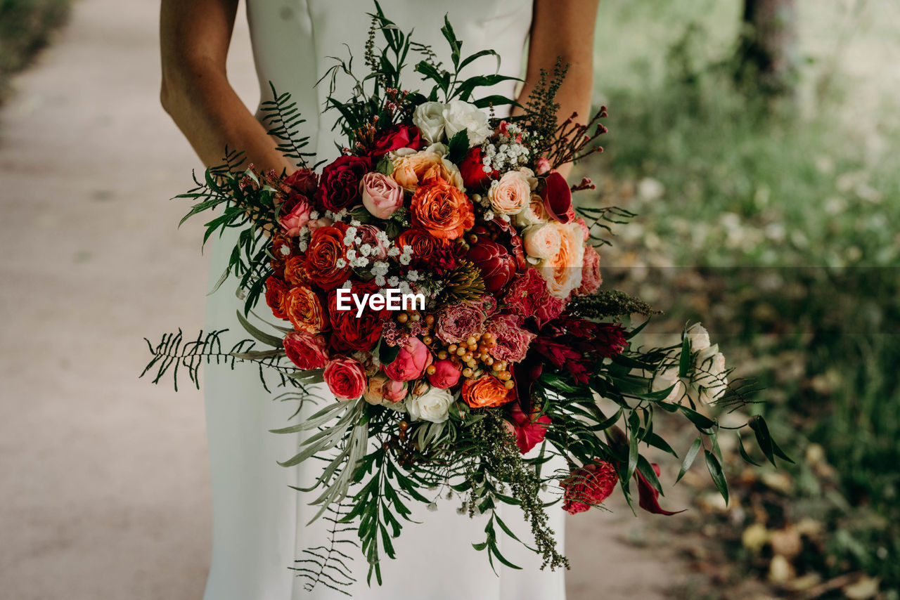 LOW ANGLE VIEW OF PERSON HOLDING FLOWERING PLANT AGAINST BLURRED BACKGROUND