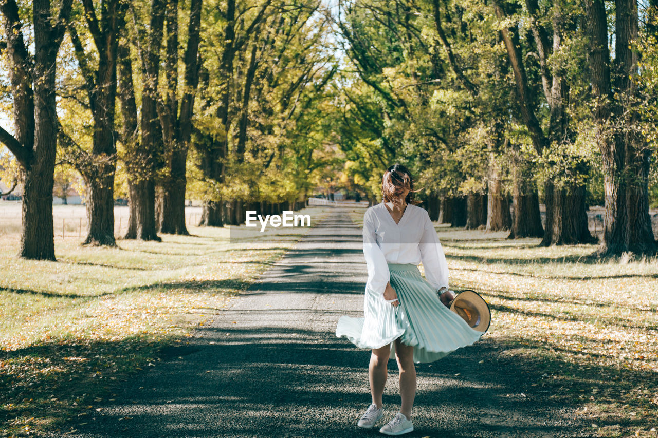 Full length of woman standing amidst trees on road