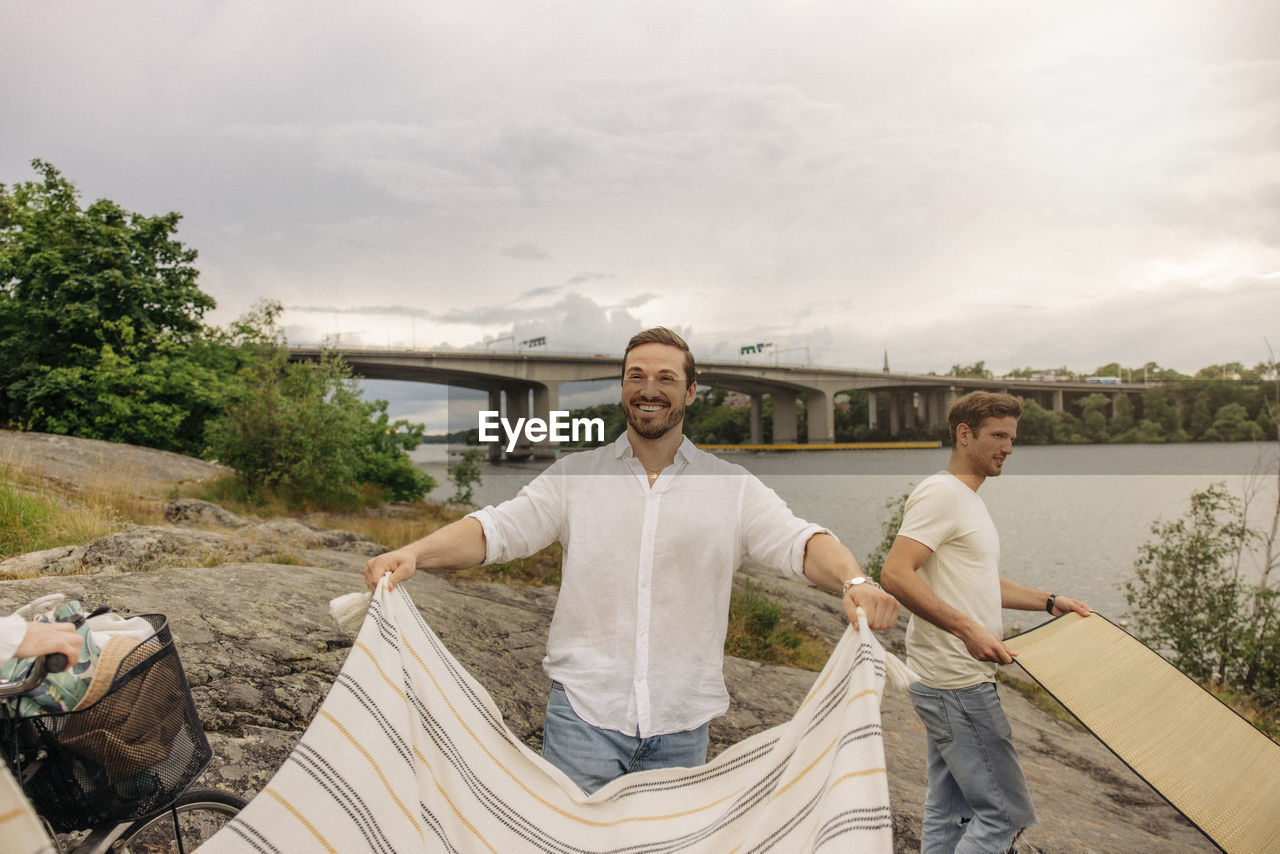 Happy man laying blanket while standing on rock during picnic