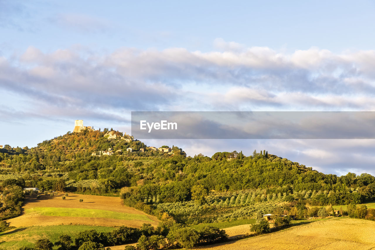 Italy, tuscany, castiglione d'orcia, clouds over rural landscape of val d'orcia with village in background