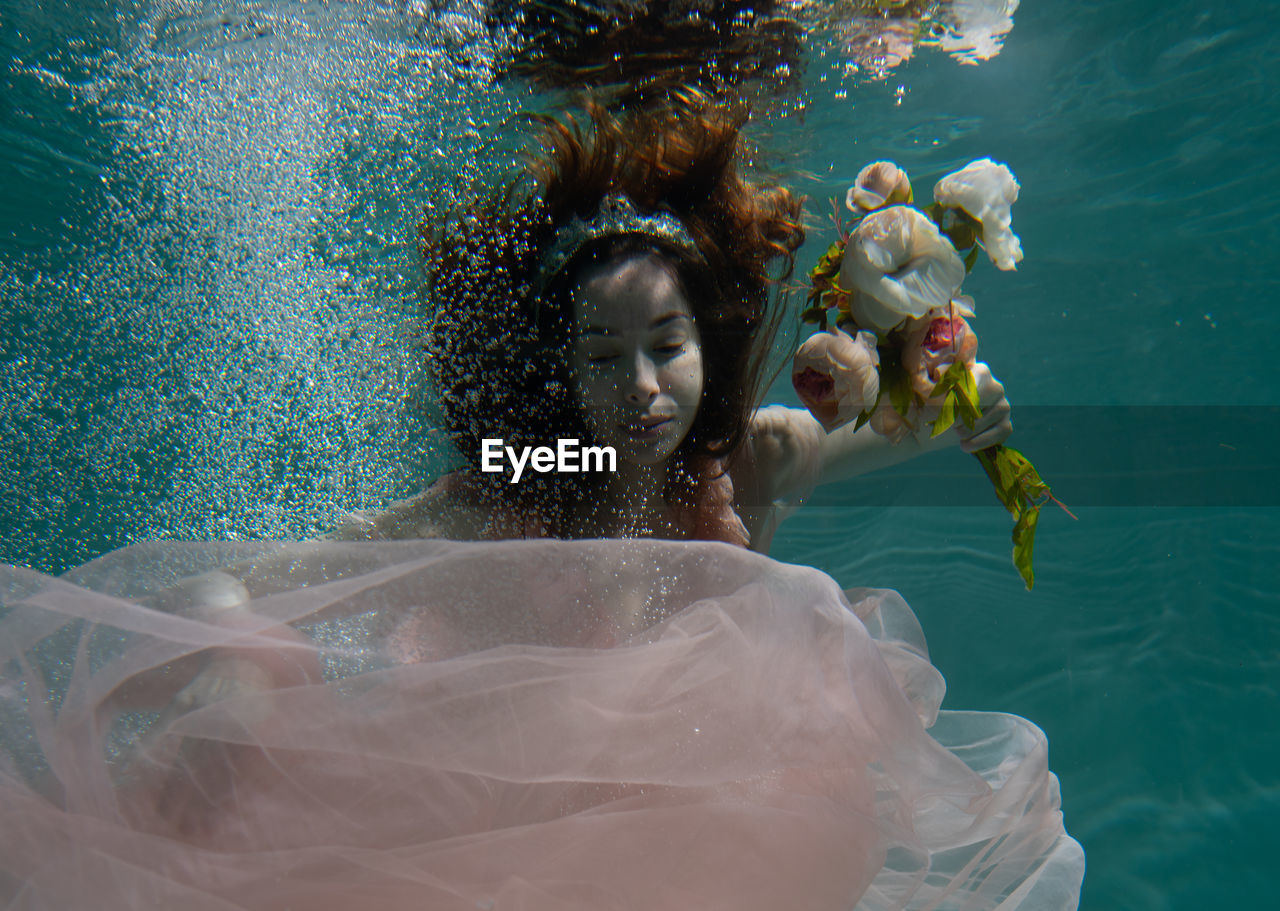 Woman holding flowers while swimming in pool