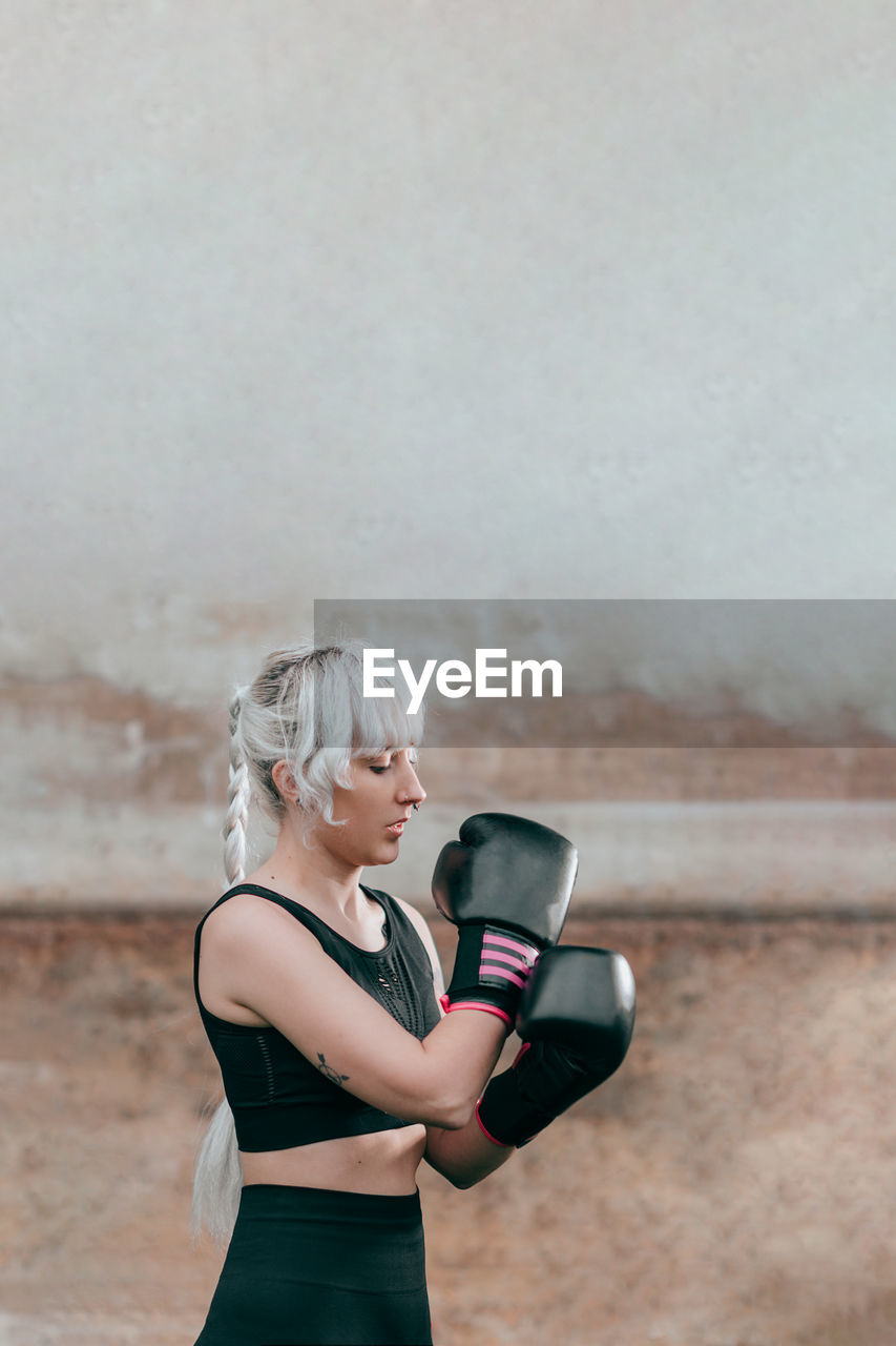 Woman with boxing gloves standing against wall
