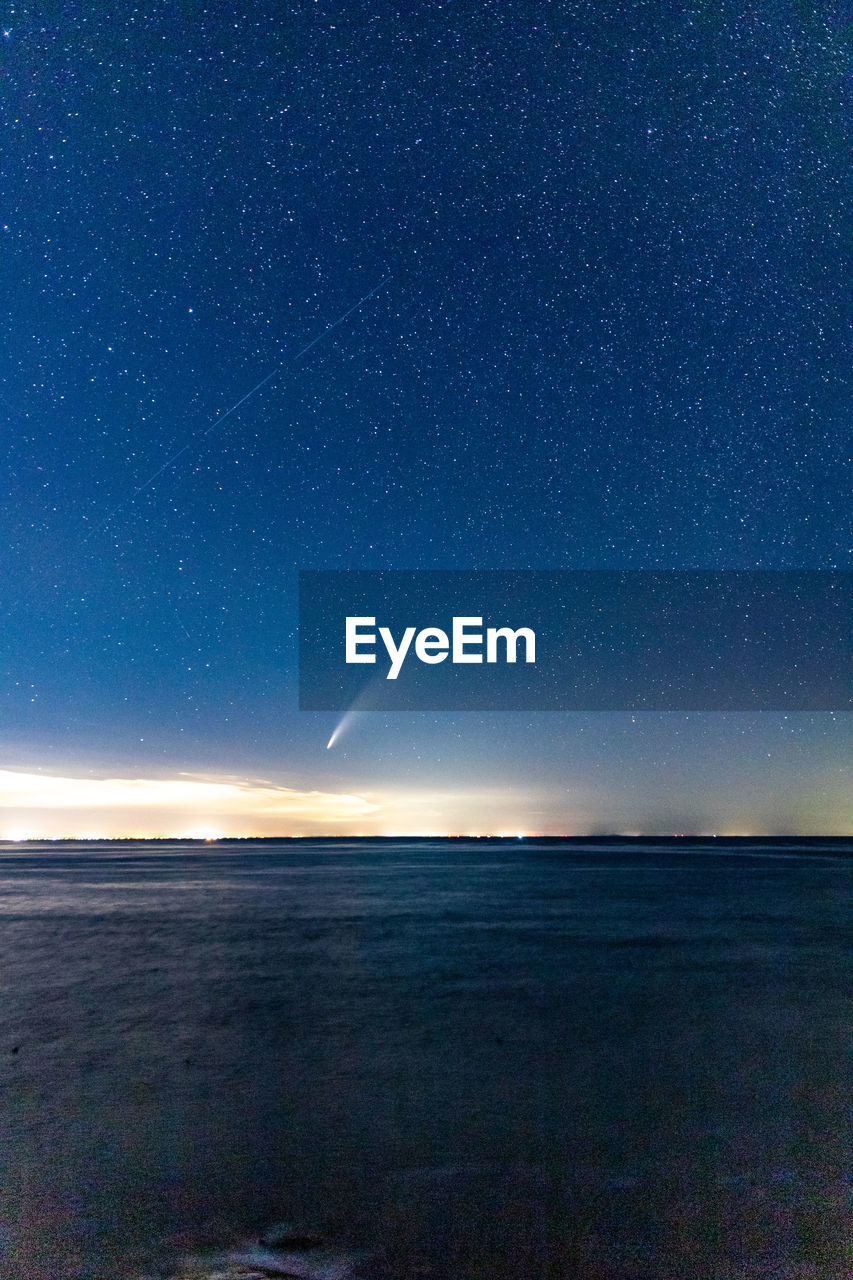 Comet neowise streaking through the starry night sky above the ocean.