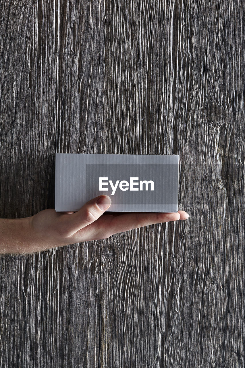 Close-up of hand holding box against wooden wall