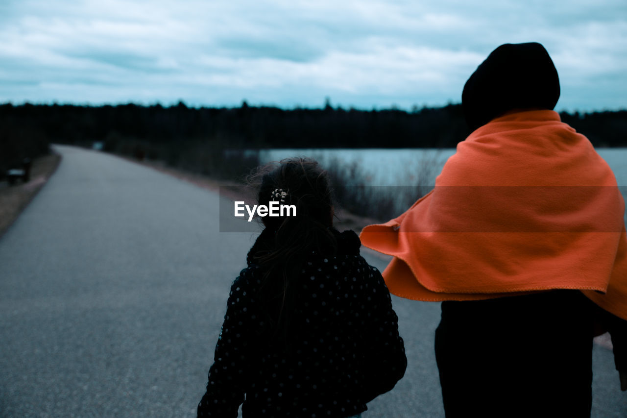 Rear view of mother and daughter standing on road during sunset