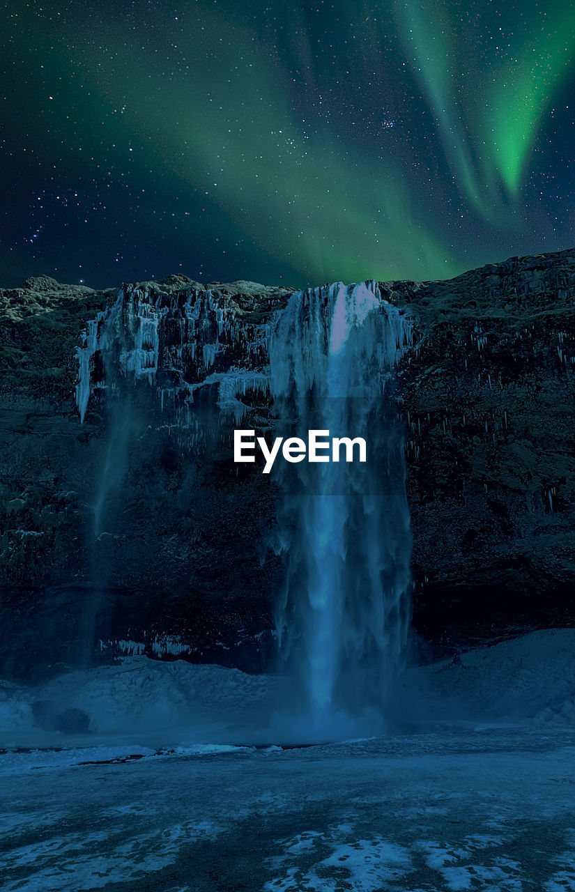 Scenic view of waterfall against aurora borealis in sky during winter