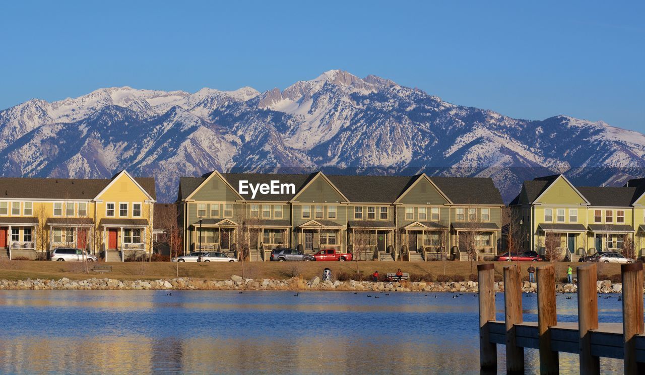 Houses by lake against clear blue sky