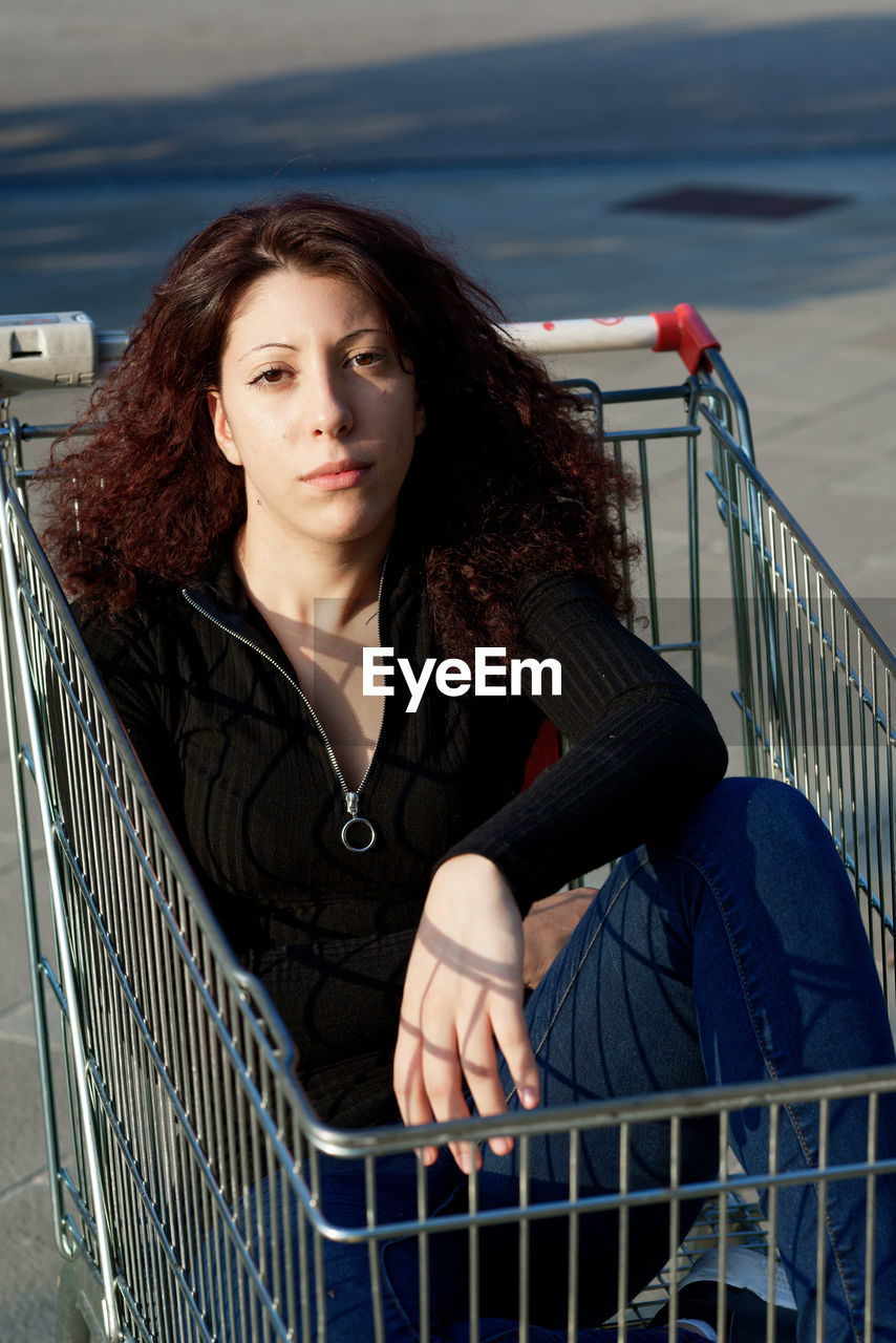 Portrait of woman sitting in shopping cart outdoors
