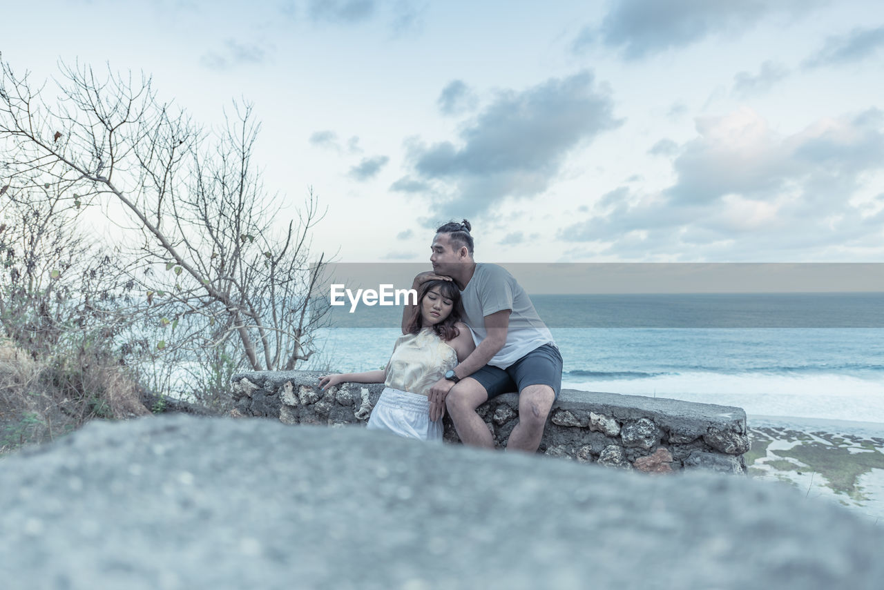 Couple embracing while sitting against sea and sky