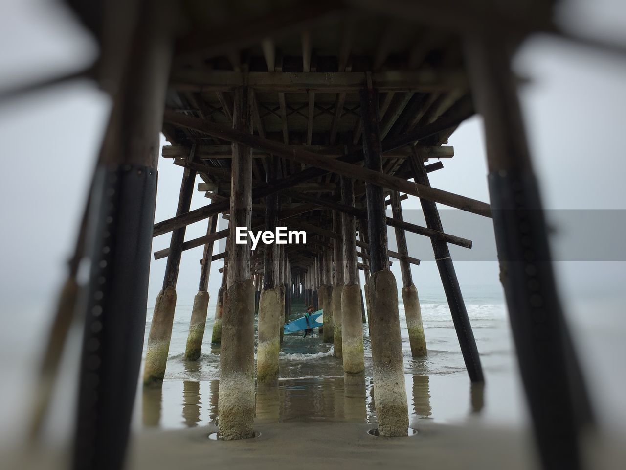 People carrying surfboard below pier in sea