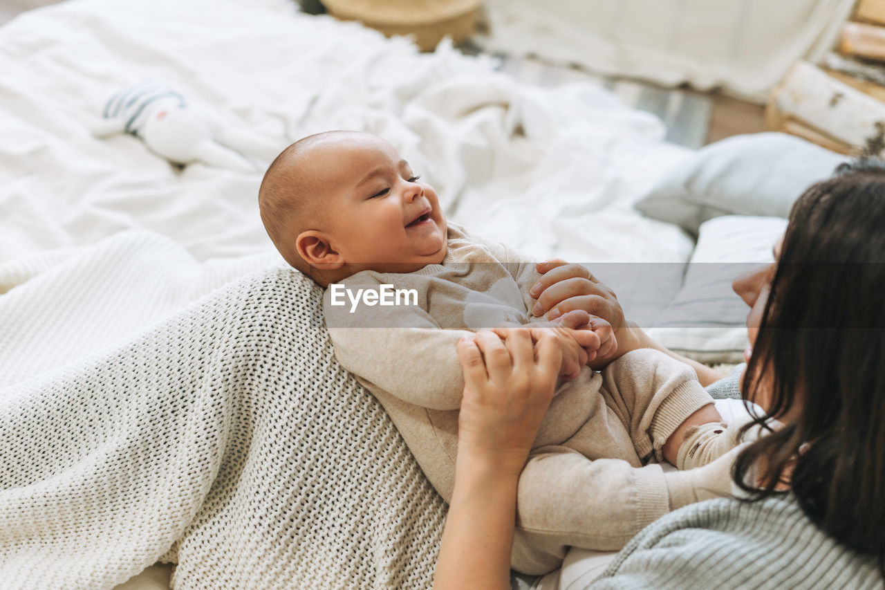 Young mother having fun with cute baby boy on bed, natural tones, love emotion