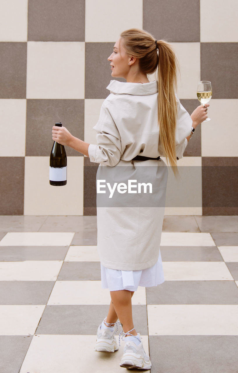 Young woman tasting white wine against chessboard background