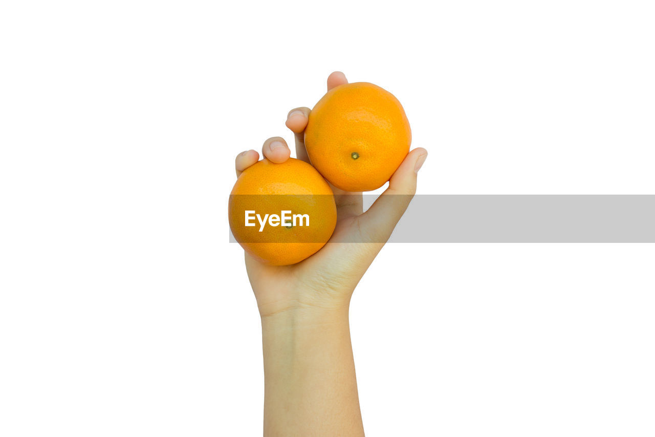 Close-up of hand holding orange against white background