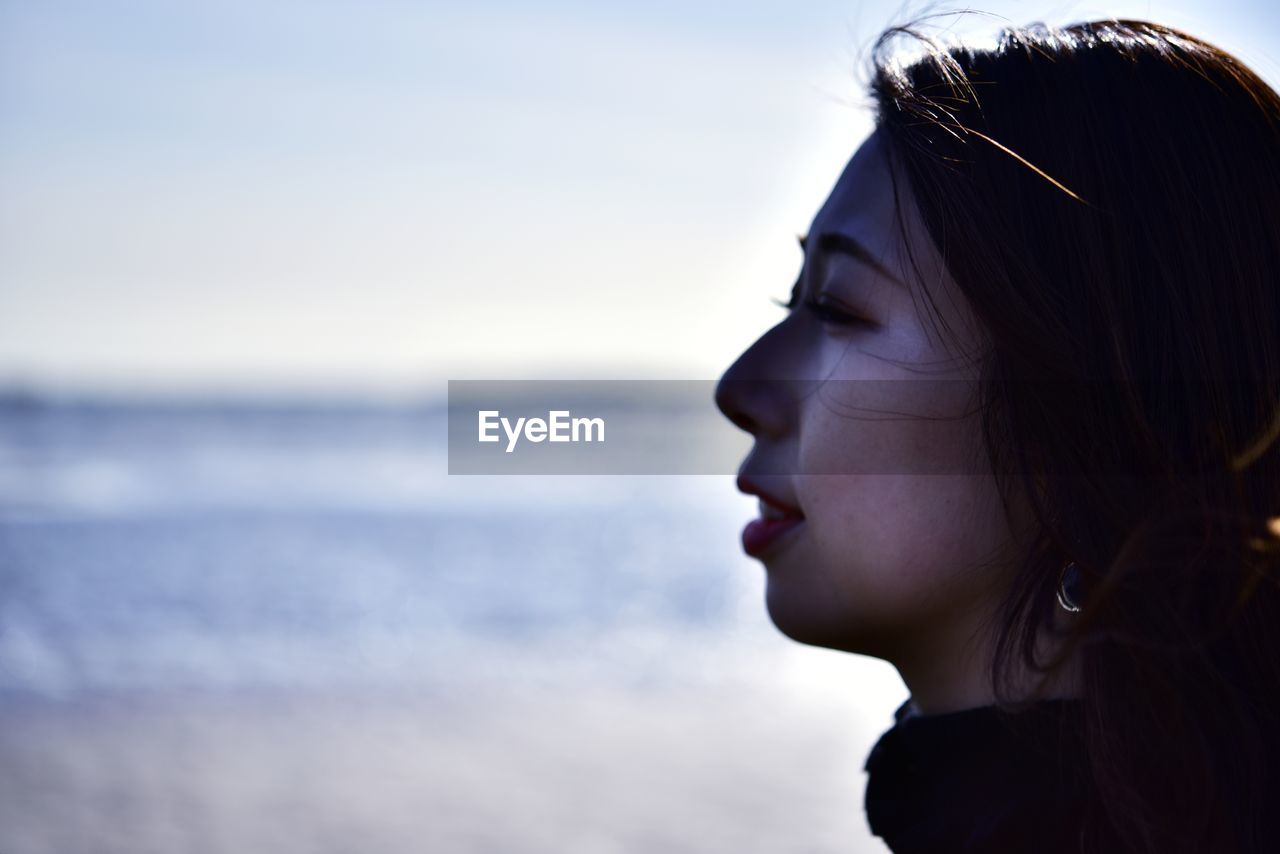 Close-up portrait of young woman looking away against sea