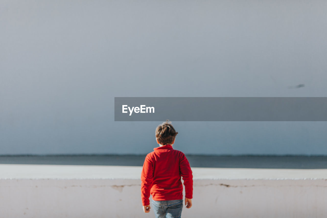 Rear view of boy standing at beach against clear sky