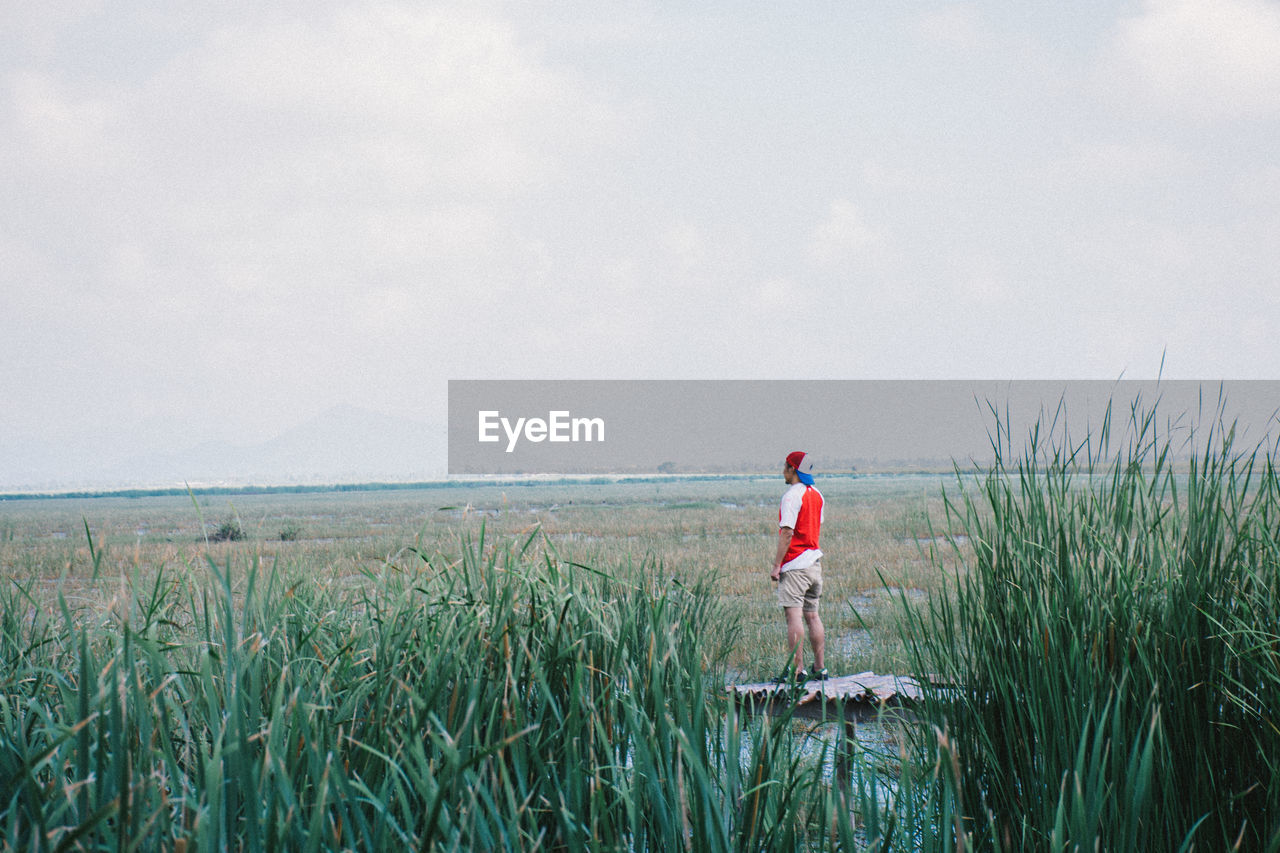 Rear view of man standing on grassy field against cloudy sky