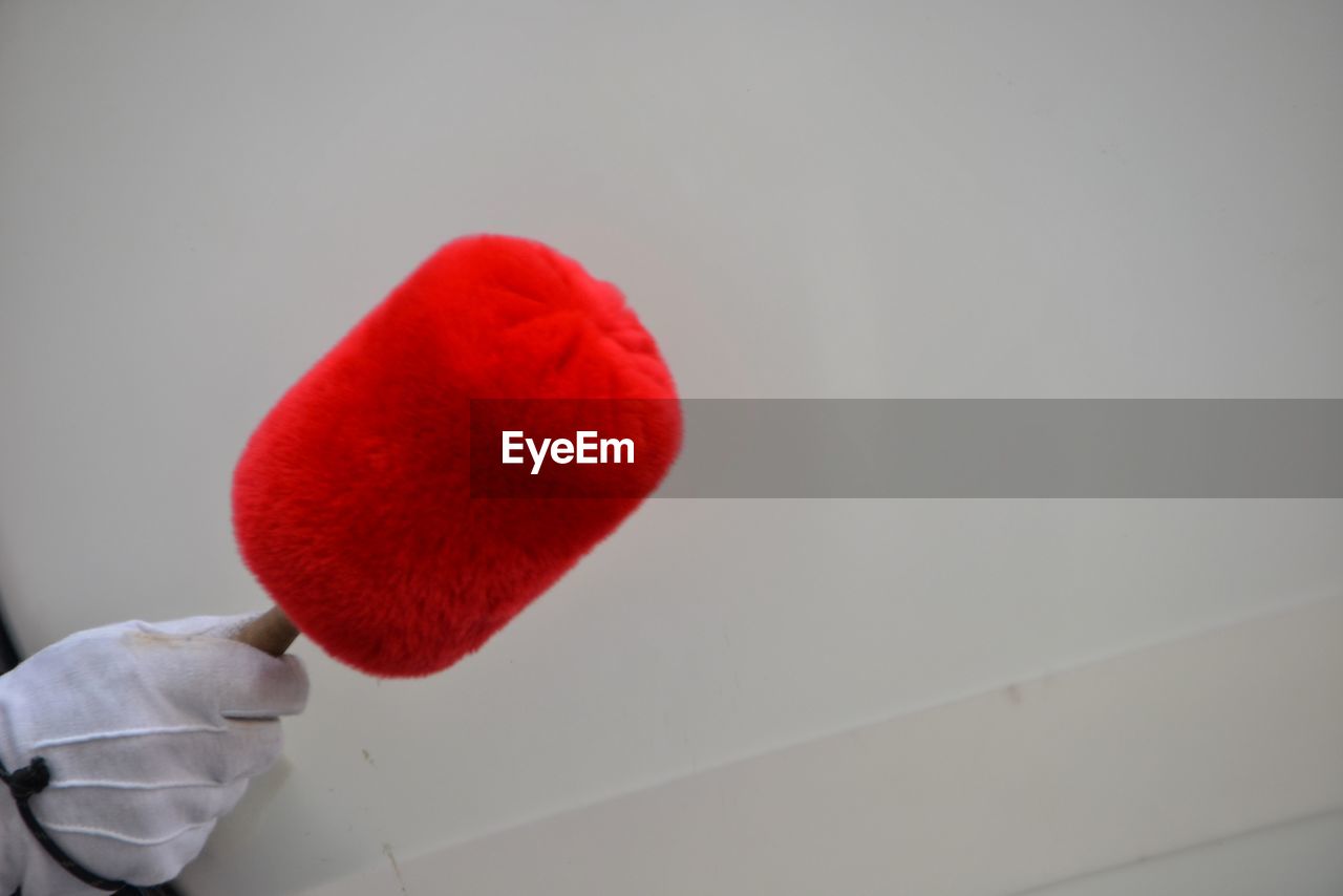 CLOSE-UP OF HAND HOLDING RED HEART SHAPE ON TABLE AGAINST WALL