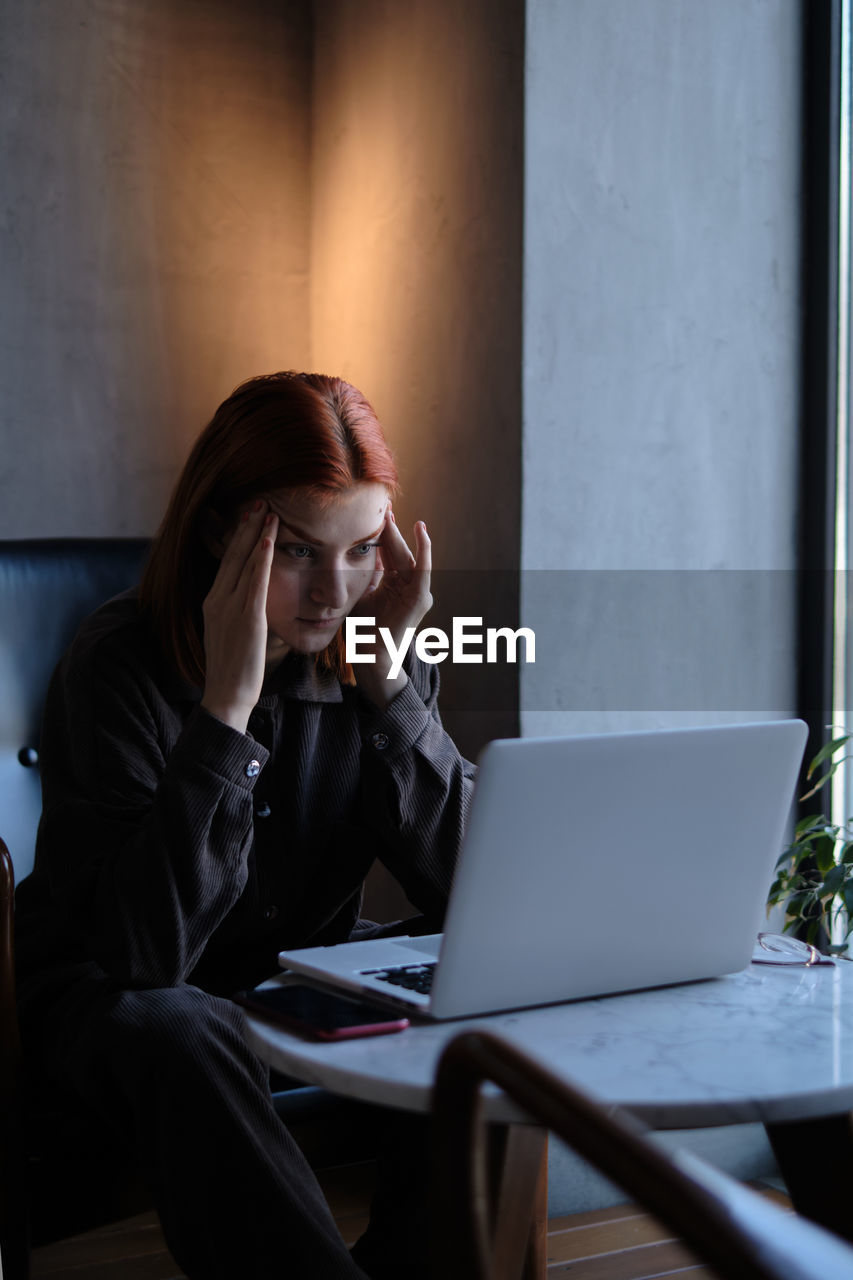 young woman using laptop while sitting on table