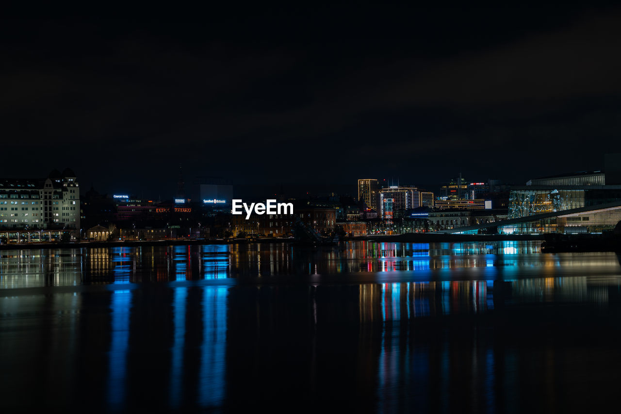 Illuminated buildings by river against sky at night