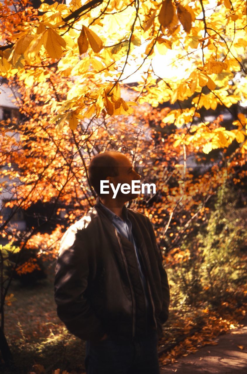 Thoughtful man standing against trees at park during autumn