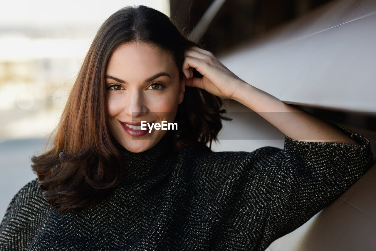 Portrait of smiling young woman by blinds