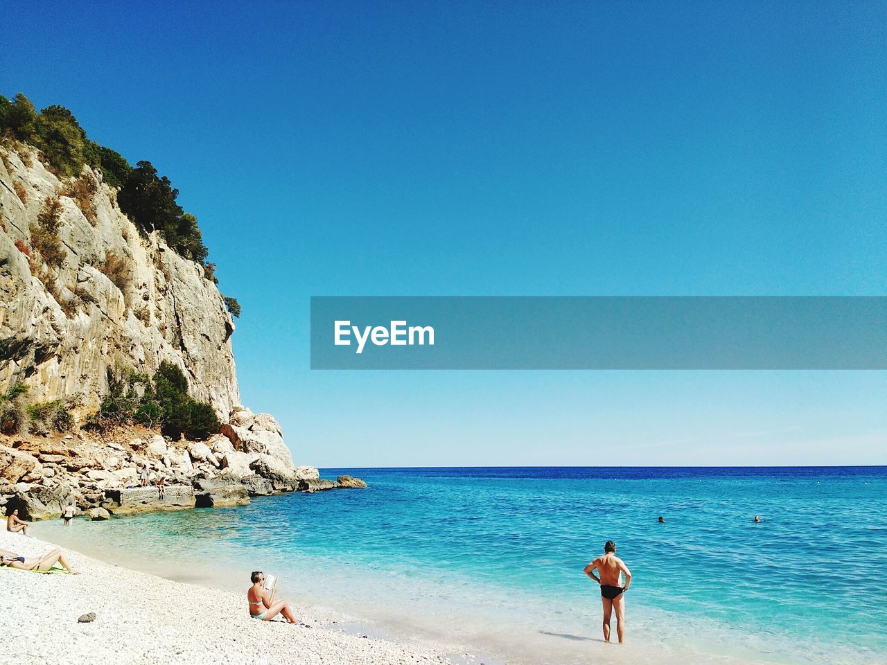 People at beach against clear blue sky