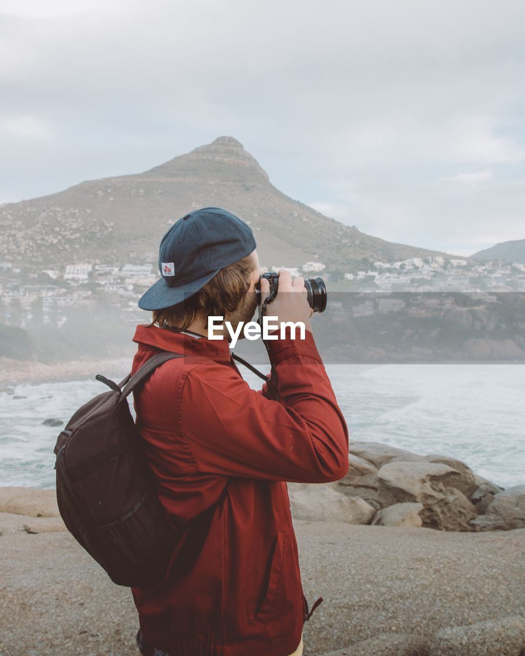 REAR VIEW OF MAN PHOTOGRAPHING AGAINST SEA