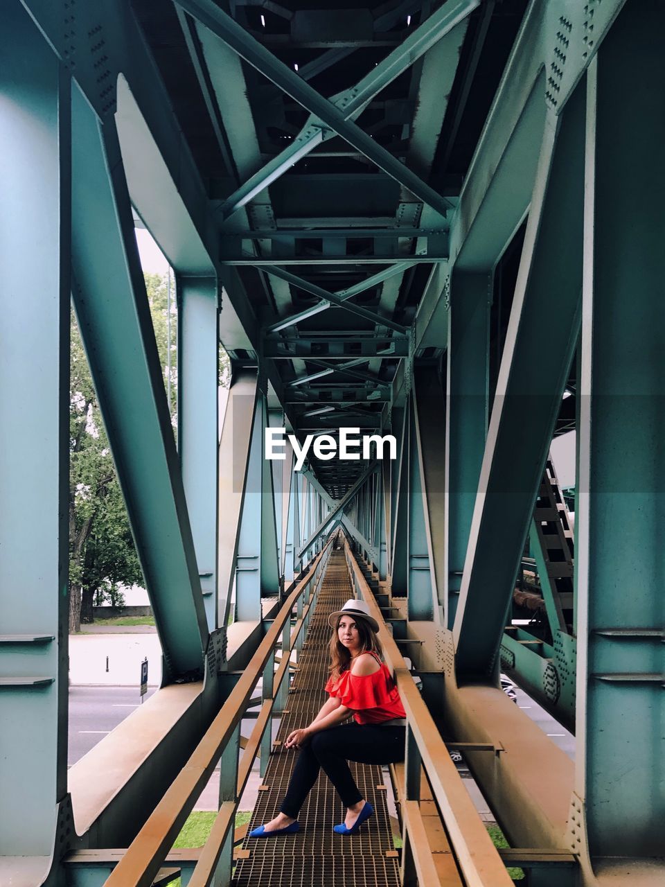 Portrait of woman sitting on railing under bridge