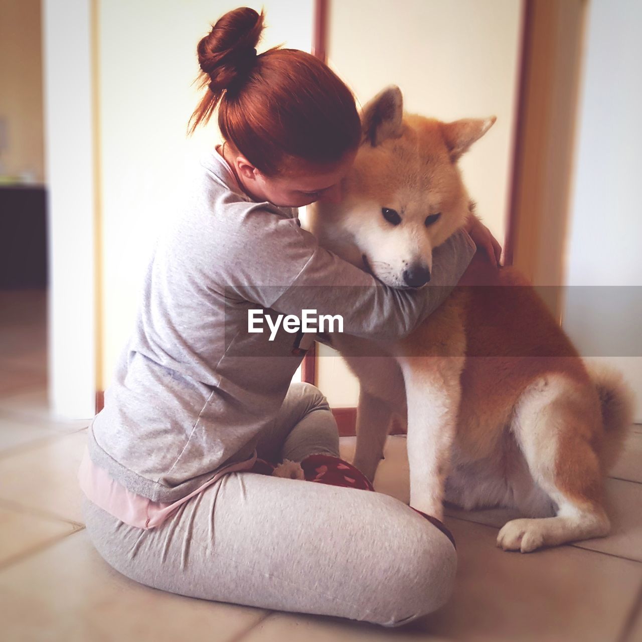 Woman embracing akita while sitting on floor at home