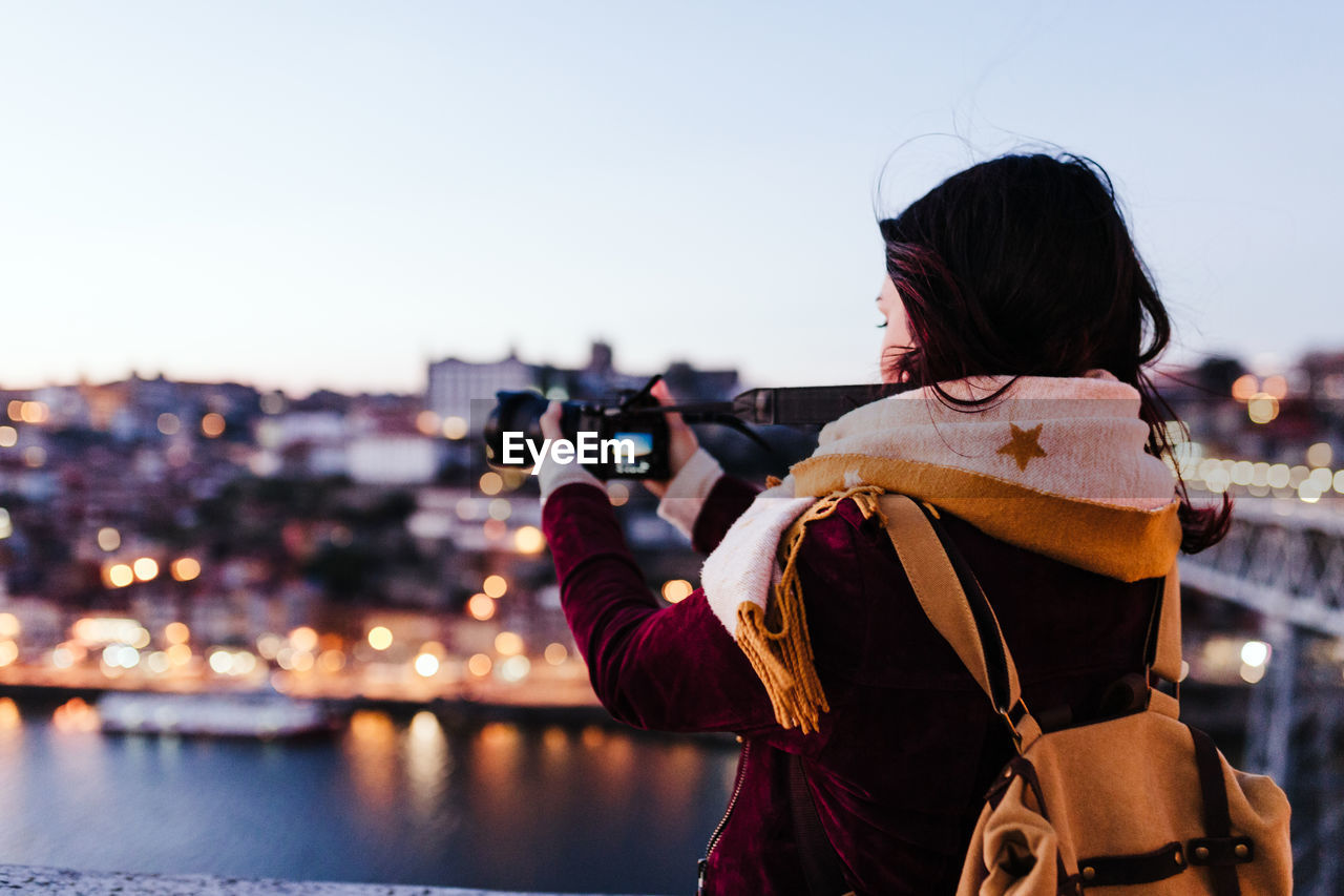 Woman in porto bridge taking pictures with camera at sunset. tourism in city europe. travel