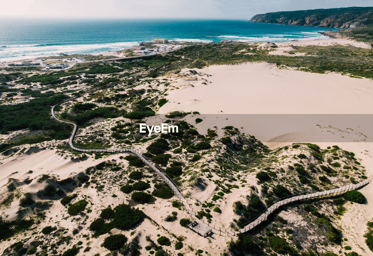 Aerial drone view of pedestrian path to guincho beach in cascais, portugal next to sand dunes.