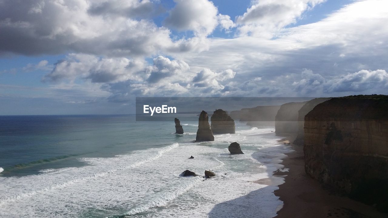 Scenic view of sea by rock formations against cloudy sky