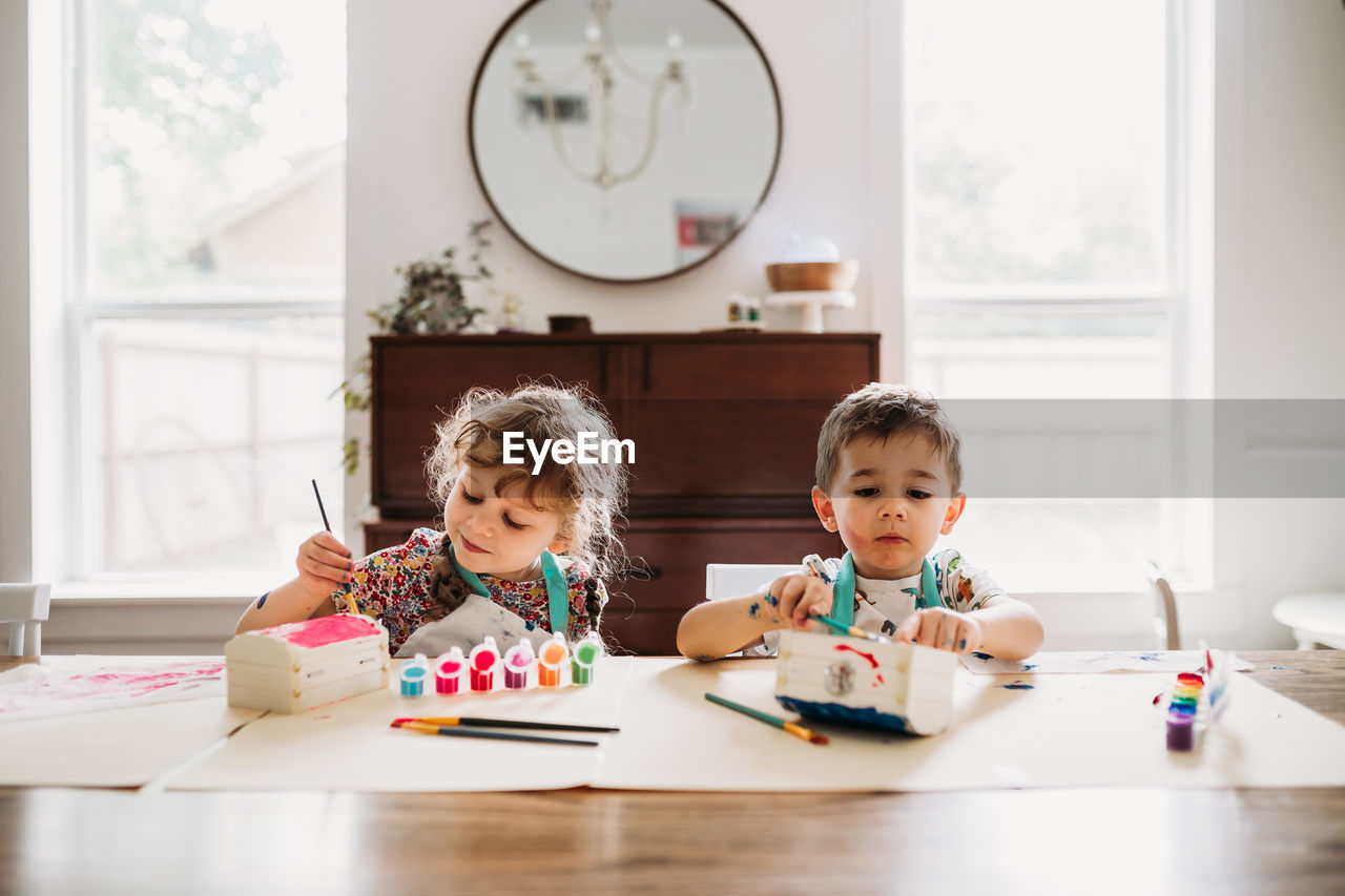 Young siblings sitting painting colorful boxes in modern dining room