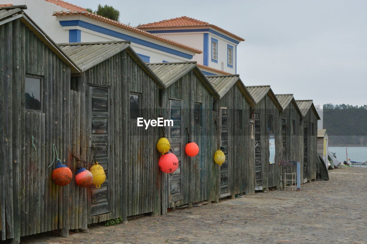 Buoys hanging on wooden houses by sea against sky