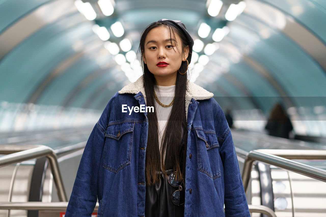 Asian girl street fashion look. stylish female wearing leather beret on escalator ride to subway