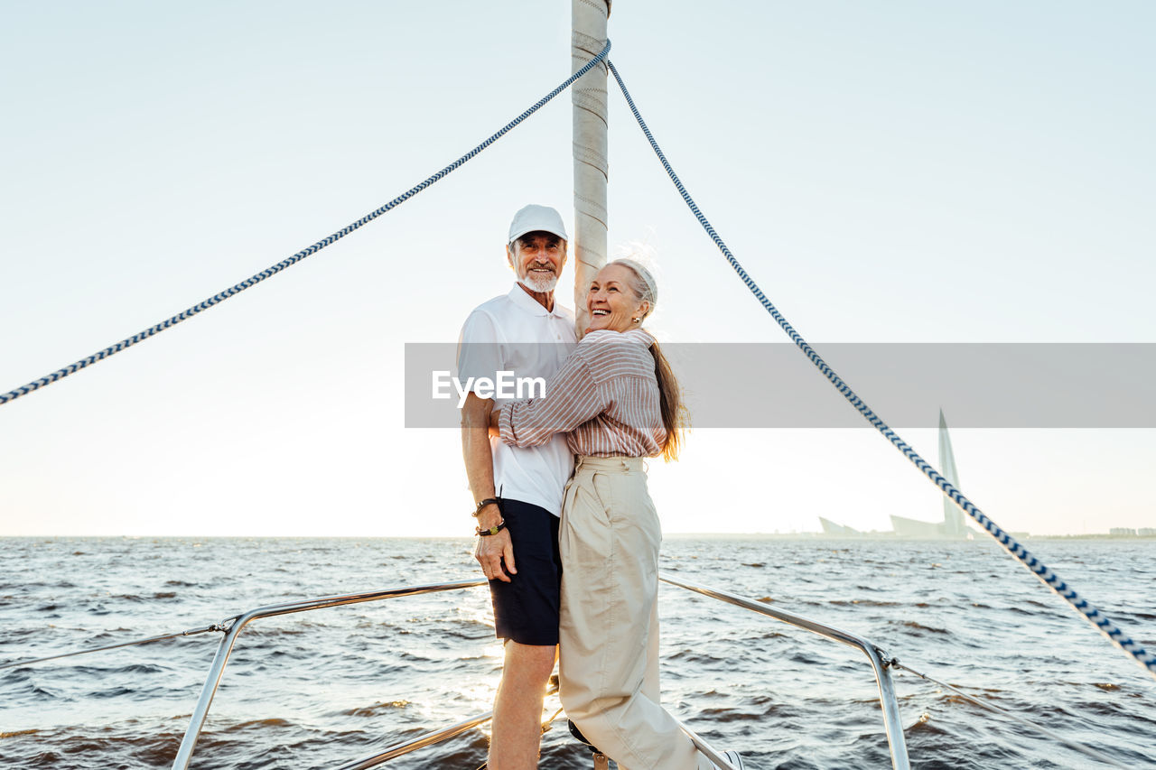 Smiling senior couple embracing in sailboat against sky