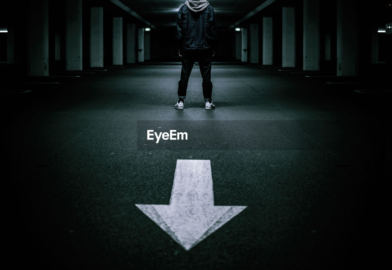 Low section of man standing by arrow symbol on road at underground parking lot