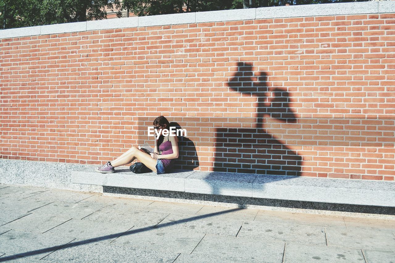 WOMAN SITTING ON BRICK WALL WITH SHADOW OF PEOPLE