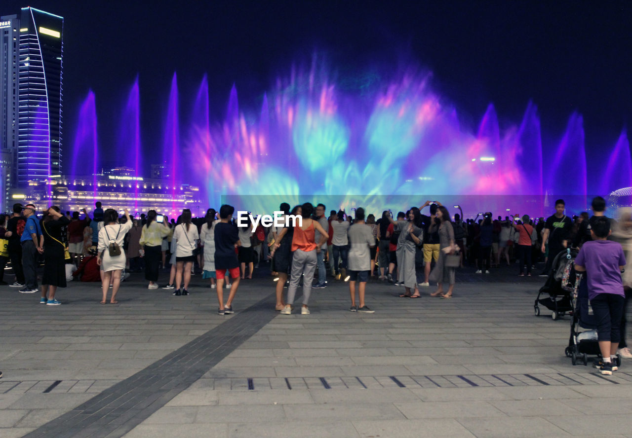 PANORAMIC VIEW OF CROWD AT ILLUMINATED STREET IN CITY