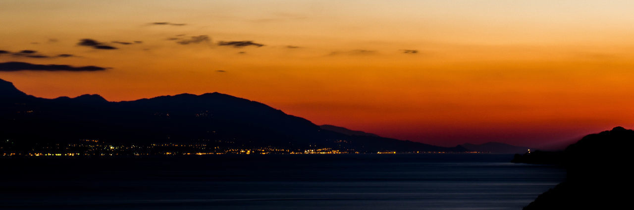 Silhouette mountains by sea against orange sky